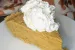 A slice of pumpkin chiffon pie topped with whipped cream. There is a cloth with fall leaves in the background.