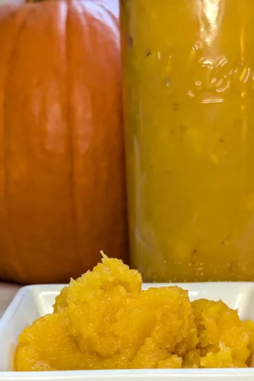 Pumpkin puree in a white dish with a jar of puree and a pumpkin behind the dish.