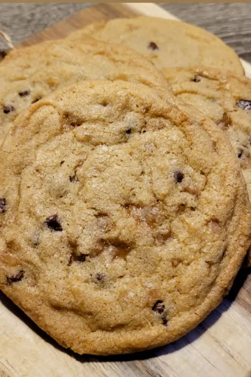 Skor chocolate chip cookies in a pile on a wood square.