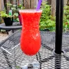 Strawberry Malibu Cocktail in a hurricane glass on a patio table. There are plants in the background.