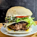 A juicy turkey burger on a white plate with cheese, lettuce and tomato.