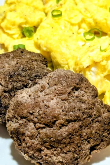 Two turkey breakfast patties on a plate with scrambled eggs and strawberries.