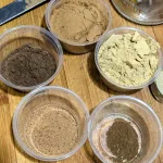 Small containers of spices to make gingerbread spice mix. Clockwise from the top: cinnamon, ginger, cloves, nutmeg, and all-spice.