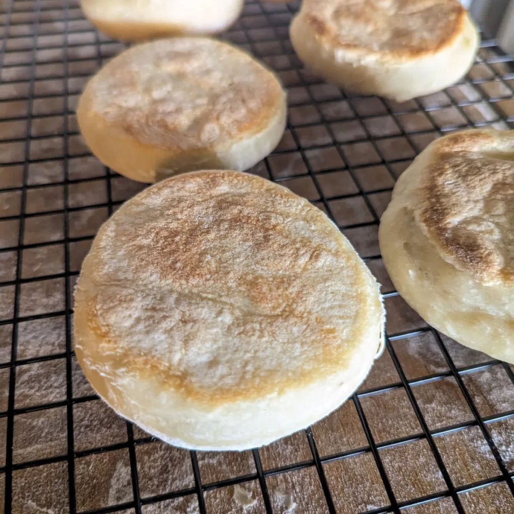 Five homemade English muffins on a wire rack.