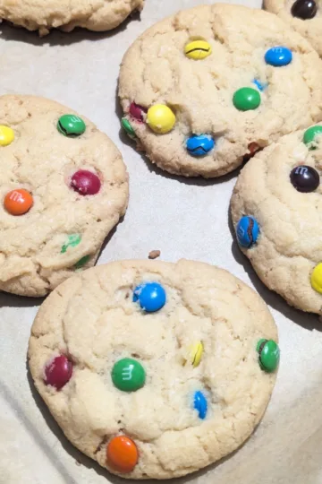A tray of M&M cookies. There are four full cookies showing with three partially visible cookies on the top edge.