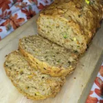 A loaf of zucchini carrot bread sliced on a wooden cutting board.