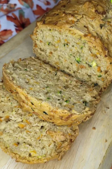 A loaf of zucchini carrot bread sliced on a wooden cutting board.