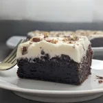 A closeup view of a piece of Canadian Whisky Brownies on a white plate with a gold fork beside it.