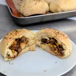 Brisket cheddar pocket cut in half on a plate with more pockets in the background.
