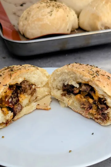 Brisket cheddar pocket cut in half on a plate with more pockets in the background.