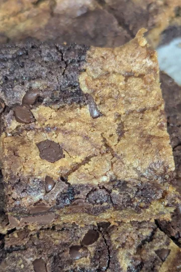 A cut square of brownie chocolate chip cookie bars sitting on top of the rest of the pan of bars.