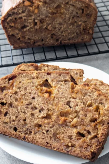 A slice of butterscotch banana bread on a plate with the rest of the loaf on a wire rack behind it.