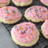 Lofthouse cookies with pink icing and sprinkles on top on a wire rack.