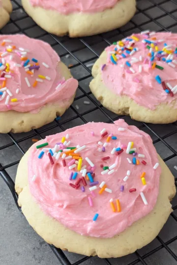 Lofthouse cookies with pink icing and sprinkles on top on a wire rack.