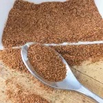 A spoonful of all-purpose seasoning on a board with a white bowl of seasoning spilled behind the spoon.