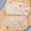 A loaf of Half Whole Wheat Bread sliced on a wooden cutting board.
