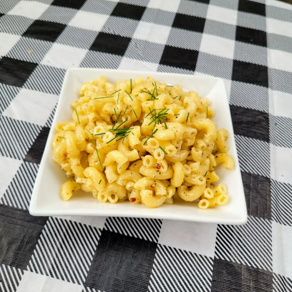 A white square bowl of copycat Kraft macaroni salad on a black and white checkered tablecloth.