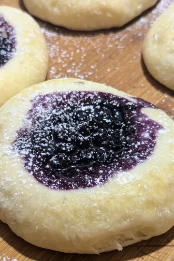 Blueberry filled kolaches dusted with powdered sugar on a wooden board.