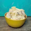 A large serving of creamy potato salad in a small yellow bowl.