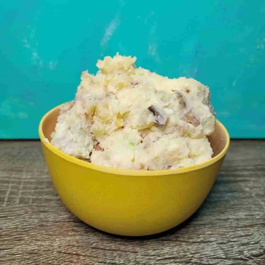 A large serving of creamy potato salad in a small yellow bowl.
