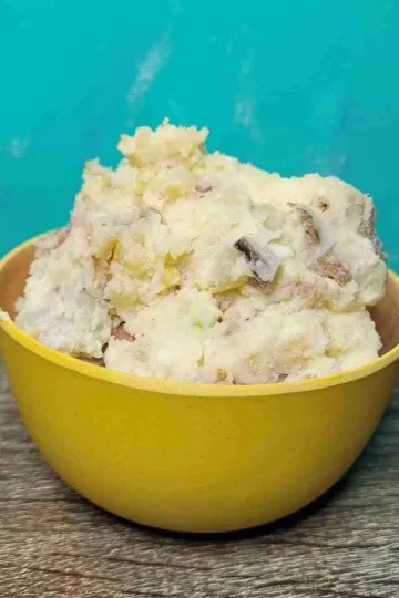 A large serving of creamy potato salad in a small yellow bowl.