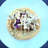 An open face fish taco on a white plate topped with coleslaw and avocado lime crema.