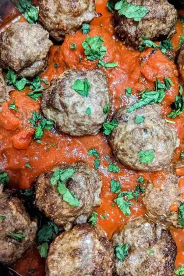 Air fryer meatballs in a pot of sauce with chopped herbs on top.