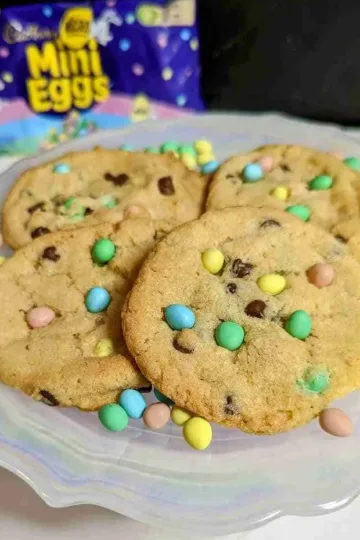 A plate with four mini egg cookies and a bag of mini eggs in the background.