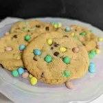 Four mini egg cookies on a plate with additional mini eggs around the cookies.