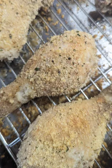 Two chicken drumsticks with homemade shake and bake on them on a wire rack.