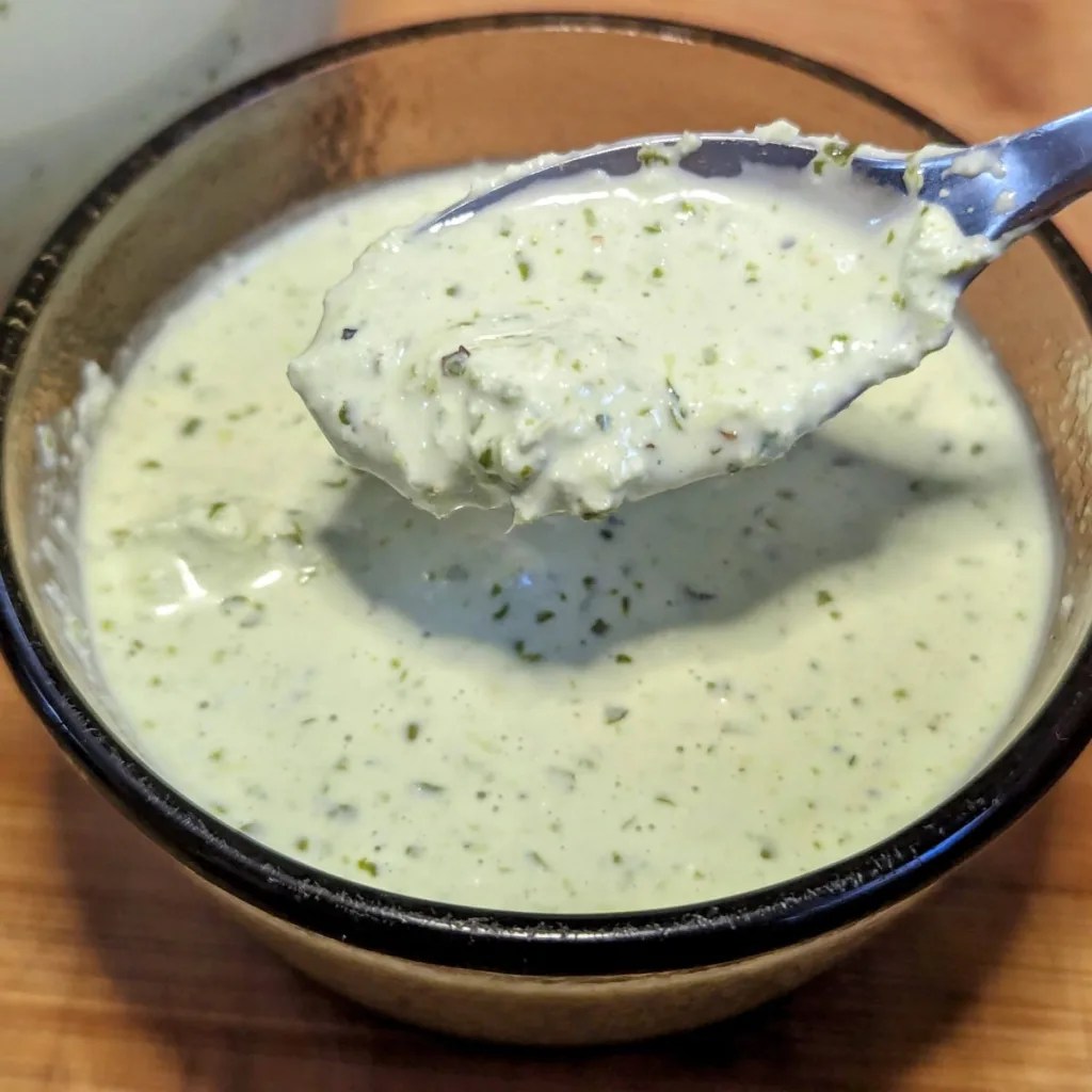 A small bowl of avocado lime crema with a spoon of sauce over the bowl.