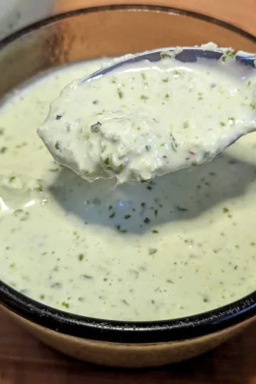 A small bowl of avocado lime crema with a spoon of sauce over the bowl.