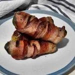 Three bacon wrapped pickles piled on a plate.