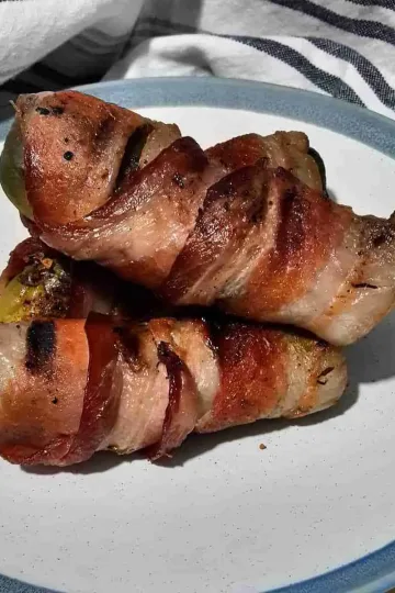 Three bacon wrapped pickles piled on a plate.
