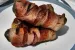 Three bacon wrapped pickles piled on a plate.