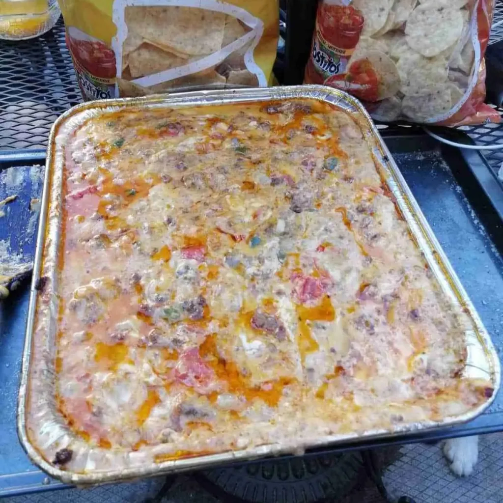 A pan of Barbecue Queso Dip with bags of tortilla chips in the background.