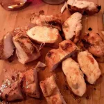 Slices of sweet chili lime chicken breasts on a wooden cutting board.