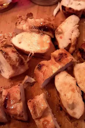 Slices of sweet chili lime chicken breasts on a wooden cutting board.