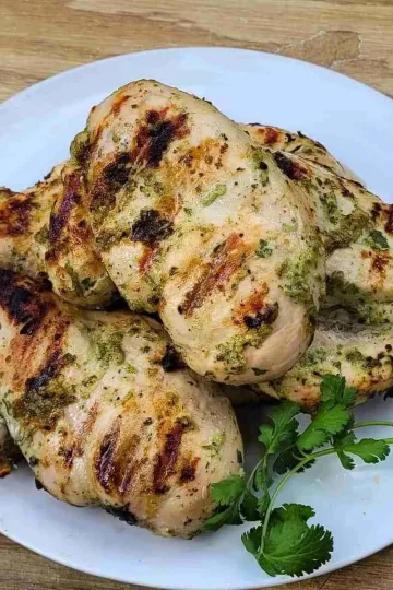 Grilled cilantro lime chicken breasts on a white plate with a sprig of cilantro on the side of the plate.
