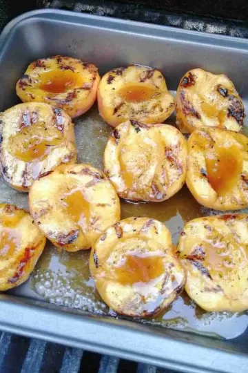 Grilled bourbon peaches in a square baking pan on a BBQ.