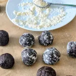 Brownie Protein Bites with a plate of almond flour and a small spoon. Five protein bites are coated in almond flour, three are plain.