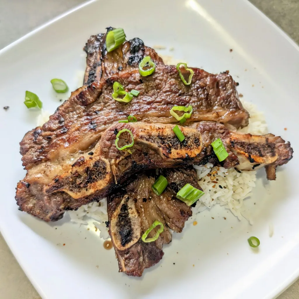 Gilled Korean Style Short Ribs on a plate of rice with chopped green onions on top.