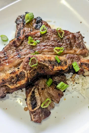 Gilled Korean Style Short Ribs on a plate of rice with chopped green onions on top.