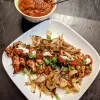 A plate of grilled chicken and onions with Ancho chile sauce poured over and a bowl of sauce in top left.