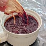 A ramekin filled with cherry BBQ sauce with a piece of chicken being dipped into it.