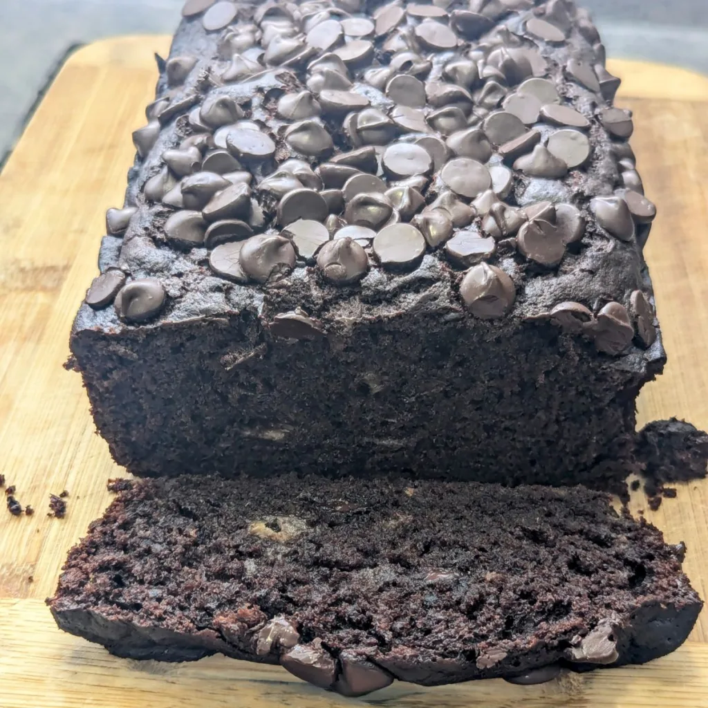 A loaf of Double Chocolate Banana Bread on a wooden cutting board with a slice cut off and lying in front of it.