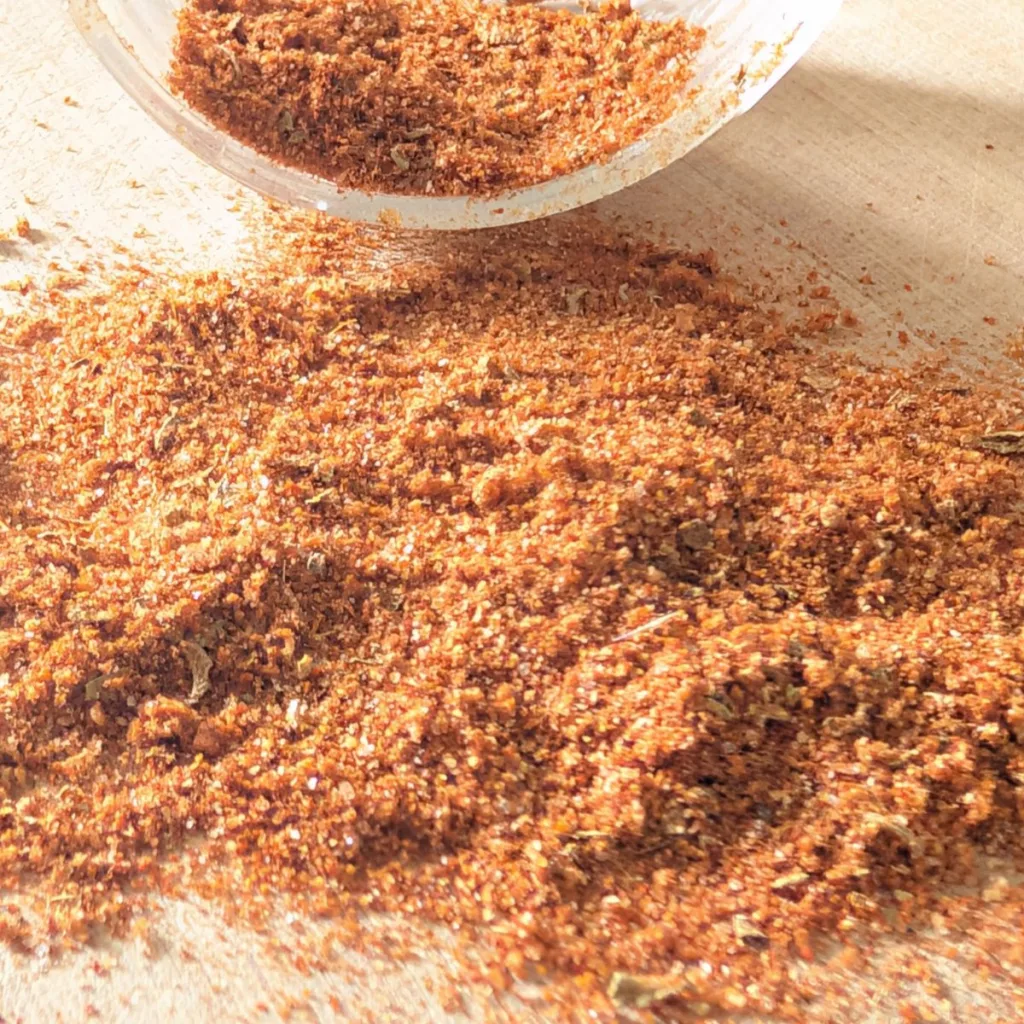 All-purpose southwest seasoning spilled on a wooden board with the opening of a jar visible behind it.