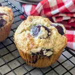 A cherry muffin on a wire rack with a red and white checkered towel behind it.