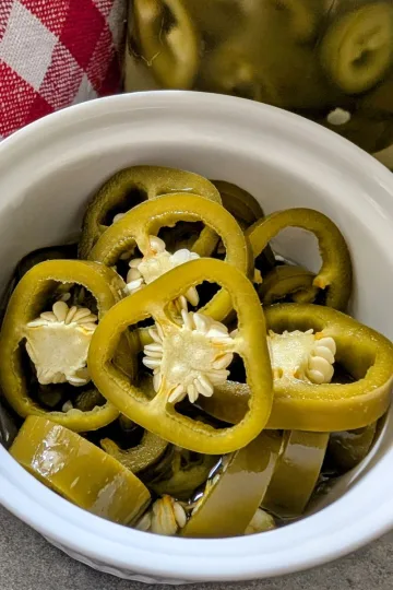 A small white ramekin filled with pickled jalapenos.