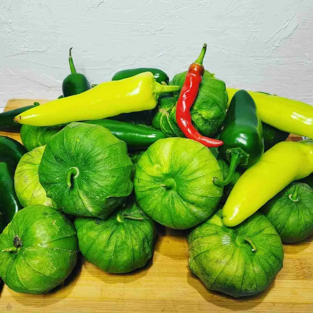 Tomatillos. jalapenos, yellow and red hot peppers on a wooden cutting board. These are the ingredients for making Tomatillo Salsa.